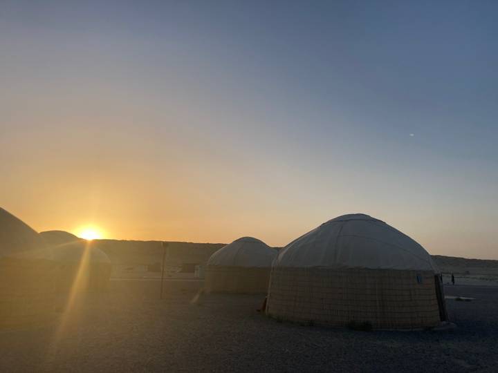 Sunset light silhouettes traditional yurts set on a desert plain.