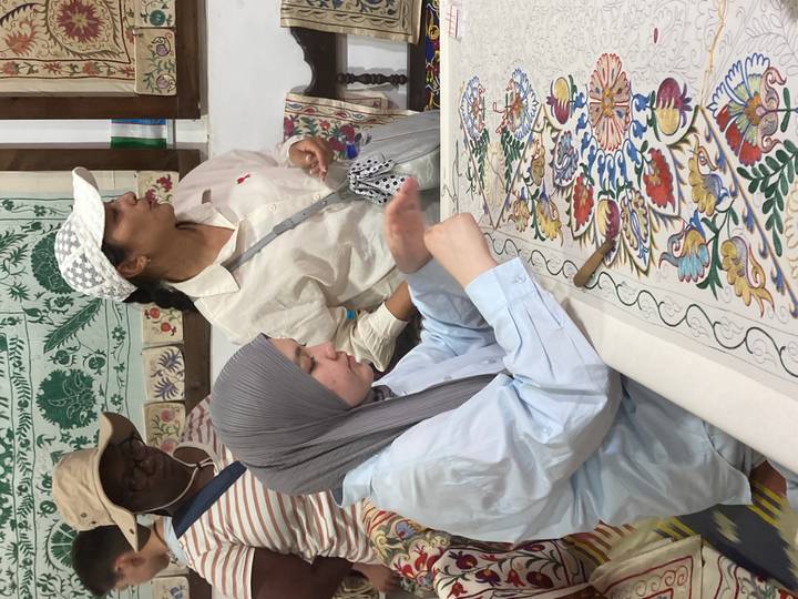 Visitors learn traditional embroidery techniques around a colorful fabric in a craft workshop.