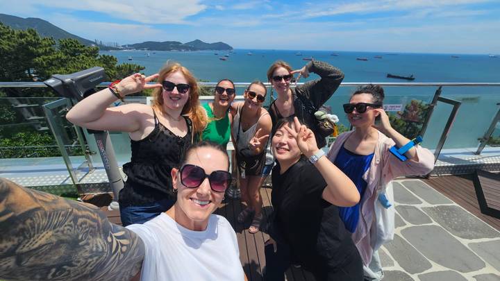 Friends take a cheerful rooftop selfie overlooking the blue sea and distant mountains on a sunny day.