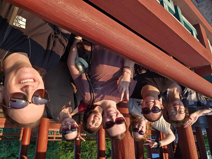 Sunset selfie of friends leaning over a red wooden bridge with warm light on their faces.