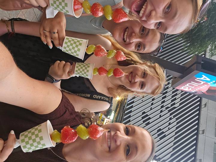 Friends show off colorful fruit skewers at a lively street market.