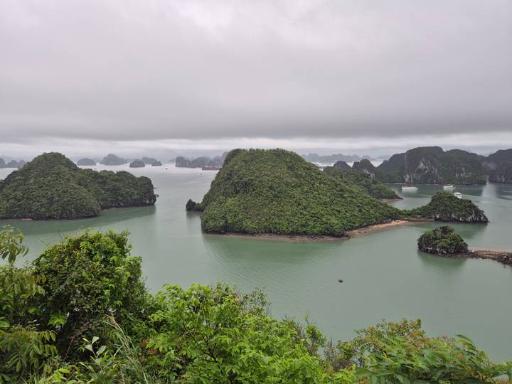 High vantage view of emerald waters and numerous lush limestone islets of Halong Bay under a low cloud ceiling.