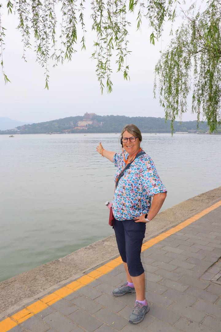 Smiling traveler pointing across Kunming Lake toward the Summer Palace on a hazy day in Beijing.