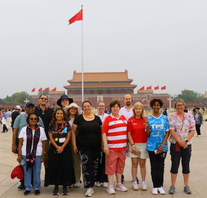 Group tour photo in front of Tiananmen Gate with red flags flying on a hazy Beijing morning.
