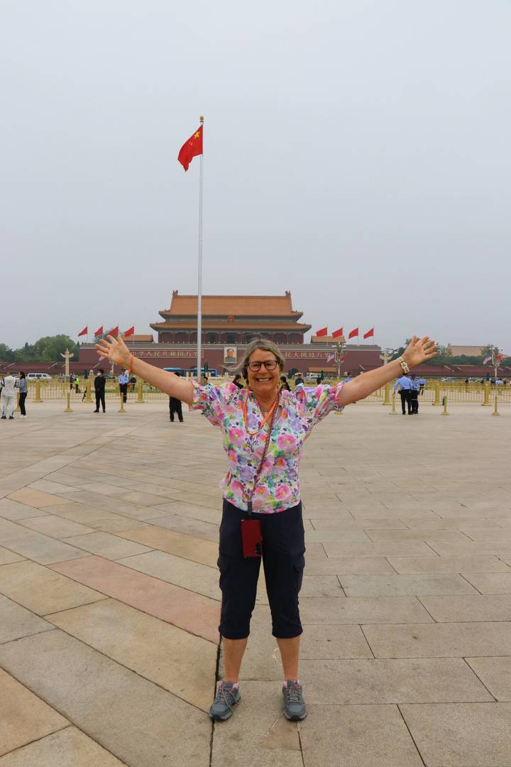 Traveler with arms raised in Tiananmen Square in front of the Forbidden City’s main gate on a hazy day.