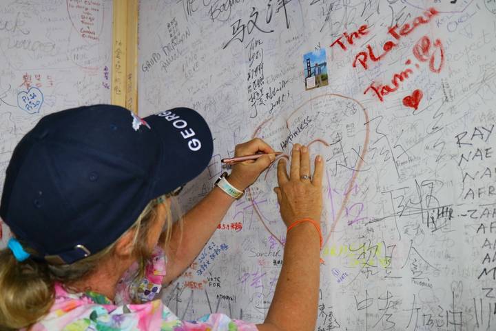 Traveler writing a message on a graffiti-covered wall filled with colorful signatures and drawings.