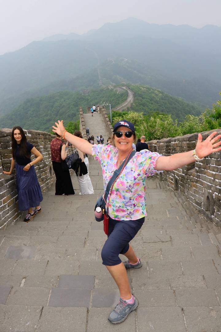 Joyful traveler stretching arms wide while walking along the stone steps of the Great Wall of China with scenic hills behind.