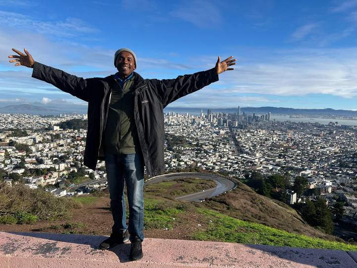 Traveler poses with arms wide atop Twin Peaks, overlooking San Francisco skyline and bay.