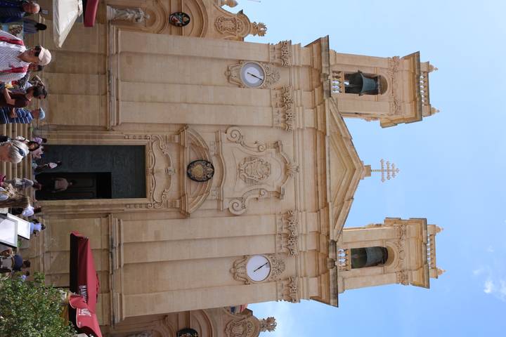 Baroque limestone cathedral facade with twin bell towers, clocks and tourists outside