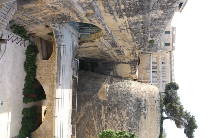 Deep limestone trench and restored fortifications in Valletta with modern bridge