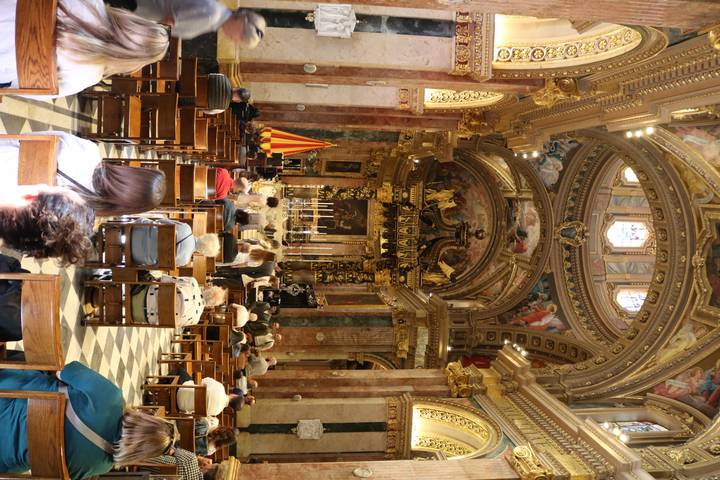 Interior of ornate baroque church with worshippers seated and gilded altar