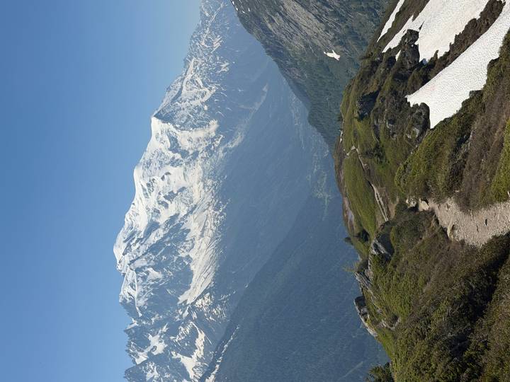 Panoramic ridge trail overlooking a deep valley and the snowy summit of Mont Blanc.