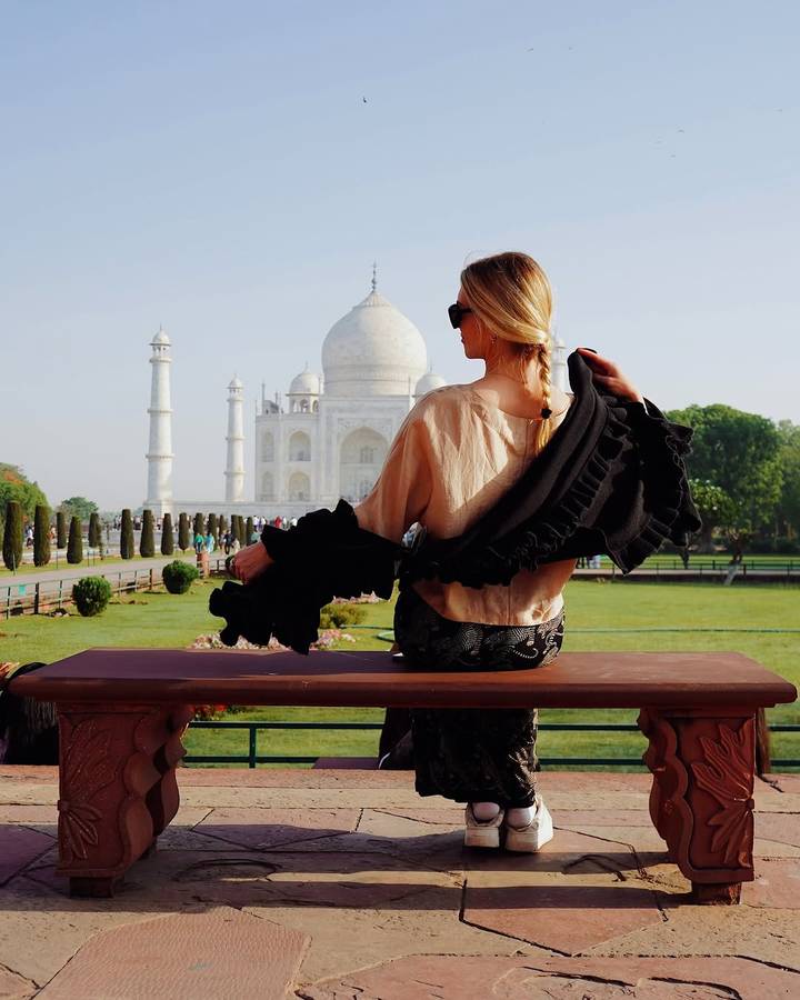 Stylish traveler admiring the Taj Mahal from a bench in the gardens.