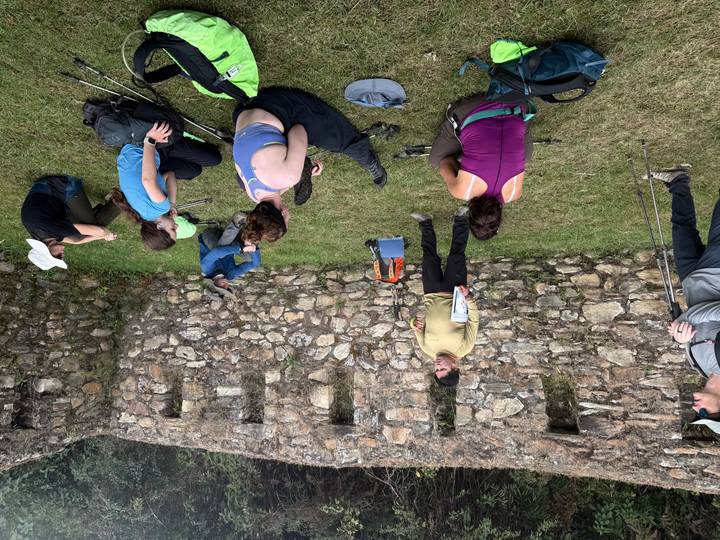 Hiking group listens to a guide beside an old stone wall during a trek briefing.