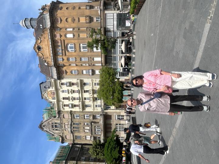 Older couple stands in a European city square with ornate historic buildings behind them.