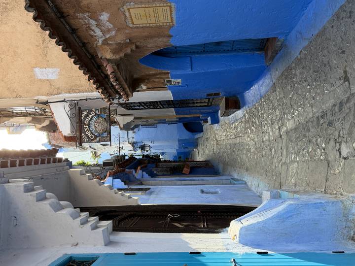Narrow cobblestone alleyway in Chefchaouen’s blue medina with rustic signage and vivid painted walls.