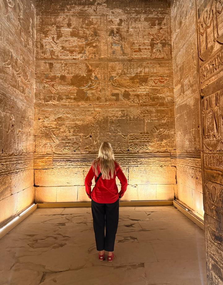 Blonde traveler admiring illuminated ancient hieroglyphs inside a temple chamber