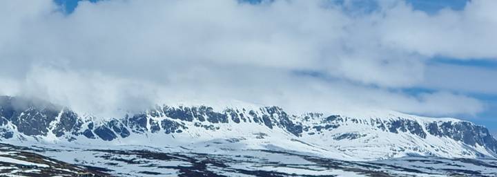 Snow-covered ridgeline half hidden by clouds in a wintry mountain landscape.