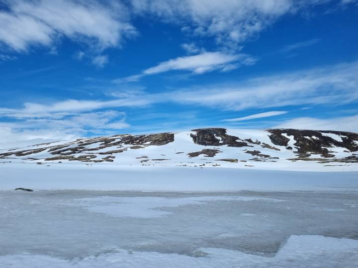 Wide snowy plateau under bright blue sky streaked with wispy clouds.