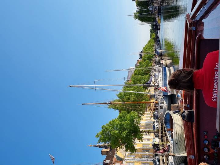 View from a small sightseeing boat cruising a leafy canal lined with masts and houses.