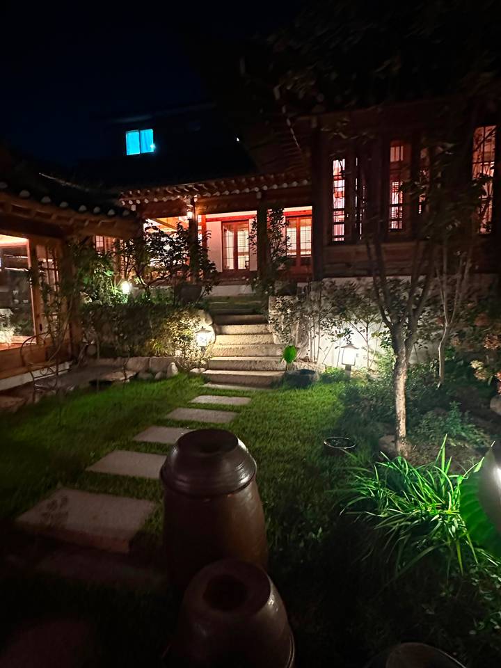 Night-time garden path with stone steps, plants and soft lantern lighting beside a hanok