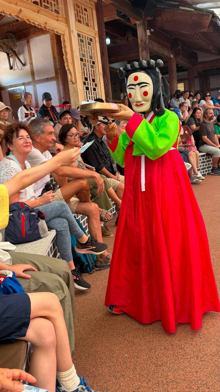 Audience seated on tiered benches watching a performer in bright traditional hanbok