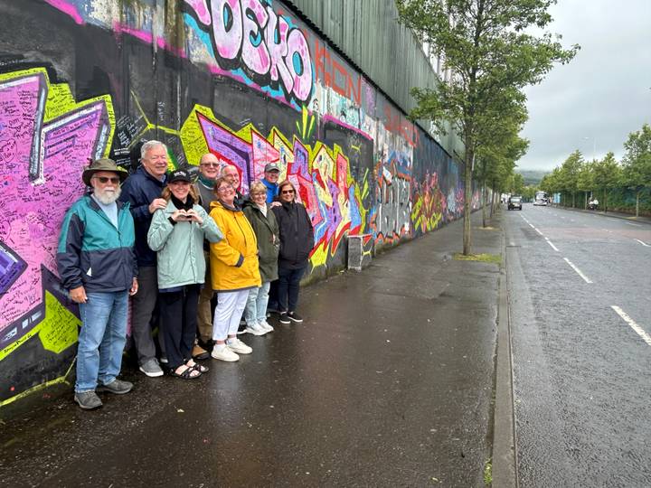 Tour group posing in front of colourful graffiti on the Belfast Peace Wall on a wet street