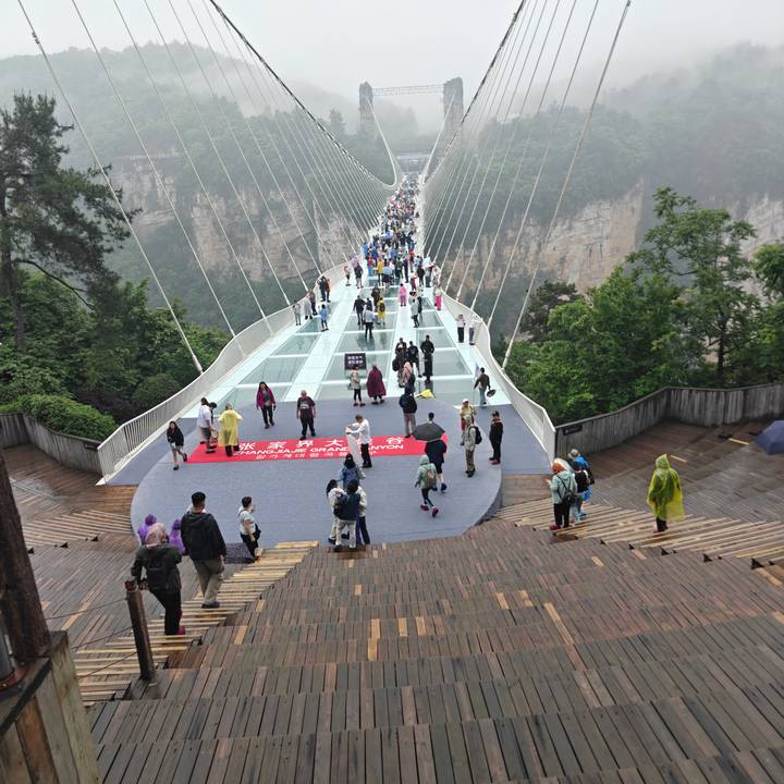 Crowds walking across the glass Zhangjiajie Grand Canyon bridge suspended above the valley