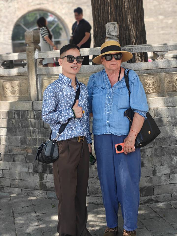 Tour guide and visitor standing together giving thumbs up near stone wall