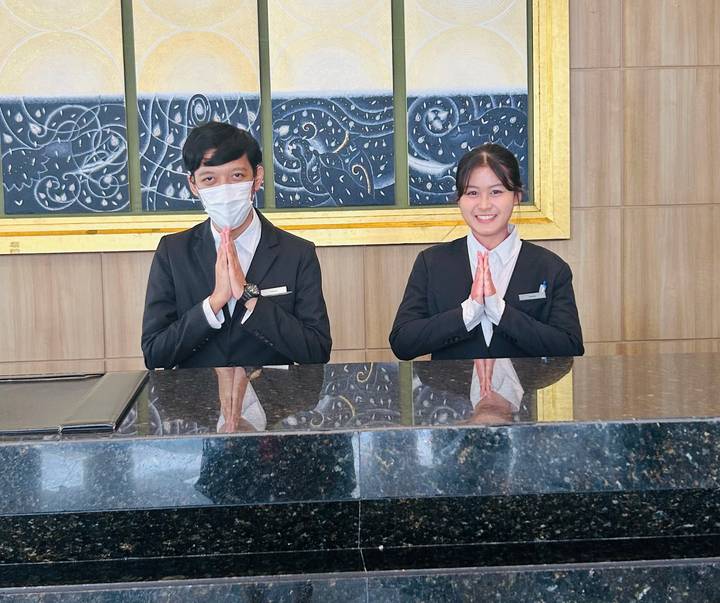 Hotel reception staff in suits greeting with palms together behind a marble counter