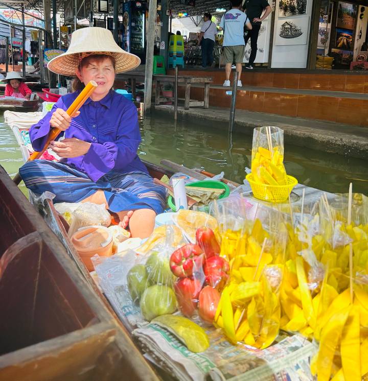 Vendor in a wooden boat sells colorful tropical fruits at a floating market canal.