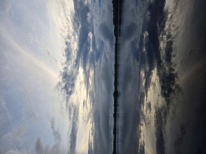 Moody twilight sky reflects on still rainforest lagoon waters creating mirror-like symmetry.