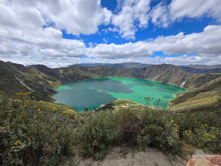 Emerald water fills the volcanic crater lake of Quilotoa under a vibrant blue sky.