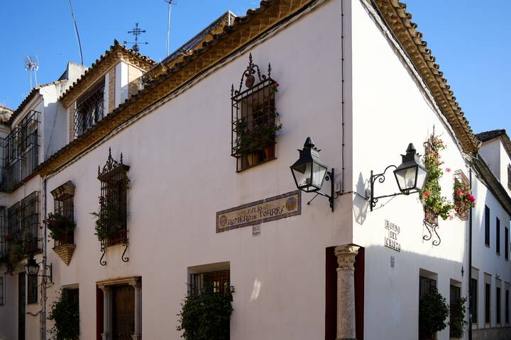 Corner view of a whitewashed Andalusian house adorned with wrought-iron balconies and flowers.