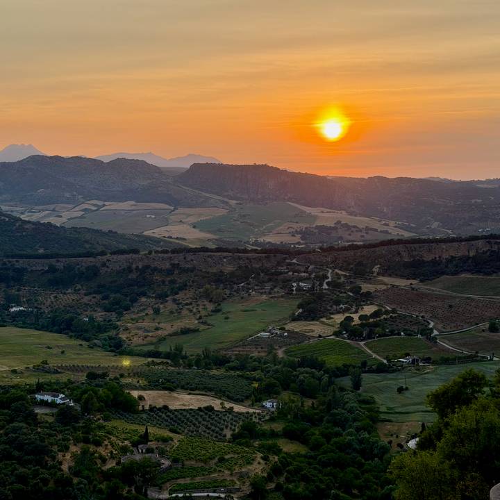 Sun setting over layered mountains and patchwork farmland in Andalusia.