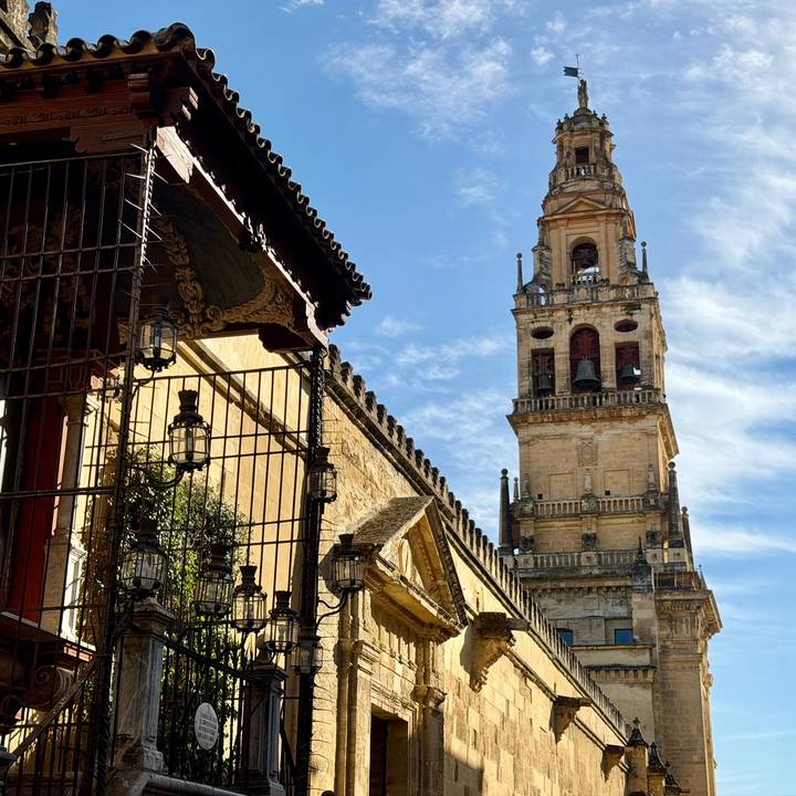 View up to the bell tower of the Mezquita-Cathedral with ornate wrought-iron gate in foreground.