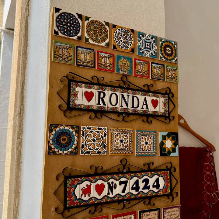 Wooden display of colourful ceramic tiles with a souvenir sign reading 'Ronda'.