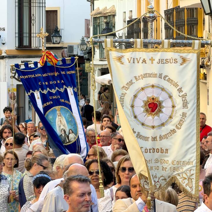 Crowded religious procession with ornate fabric banners bearing sacred images and text.