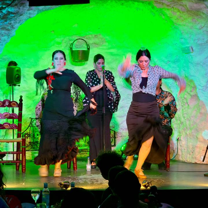 Three female flamenco dancers in vibrant lighting captured mid-movement on stage.
