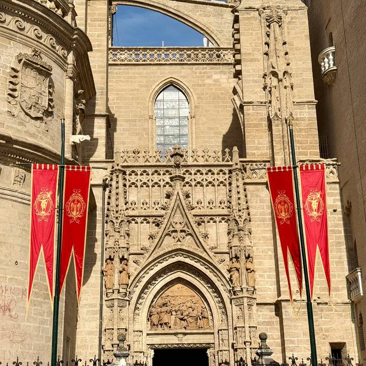Cathedral façade draped with red banners under strong morning light.