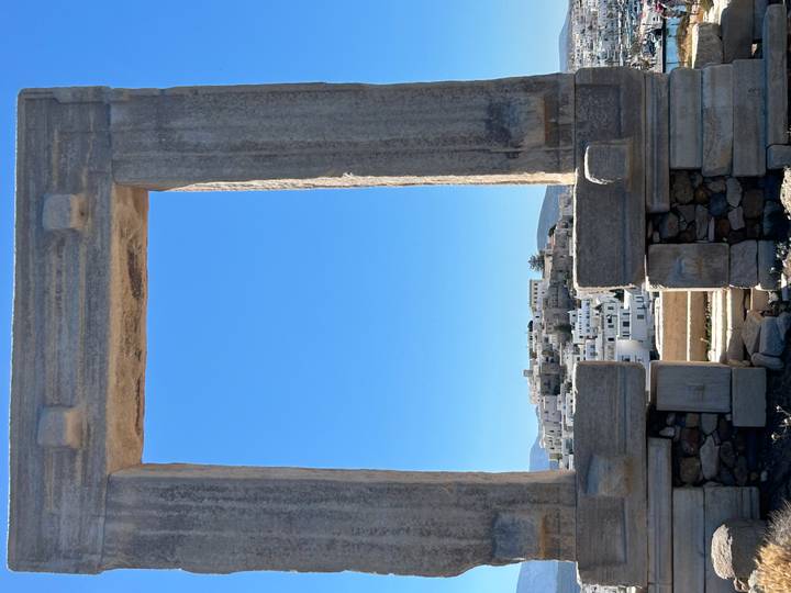 Ancient marble gateway ‘Portara’ framing the old town of Naxos against a bright blue sky.