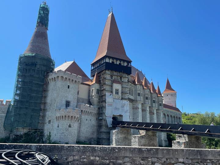 Medieval Corvin Castle with tall pointed towers, some sections under restoration scaffolding.