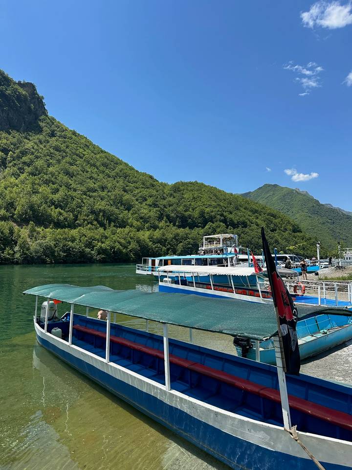 Tour boats dock beside emerald lake surrounded by steep green mountains under a clear blue sky