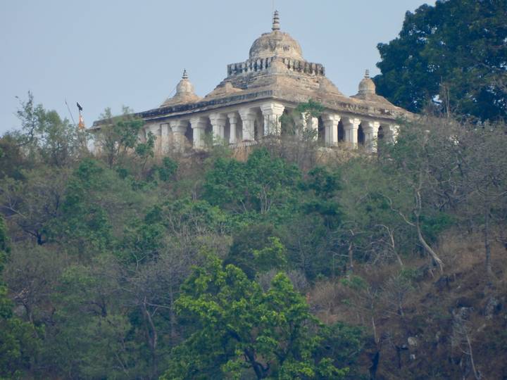 Temple-like stone structure perched on a wooded hillside surrounded by dense greenery.