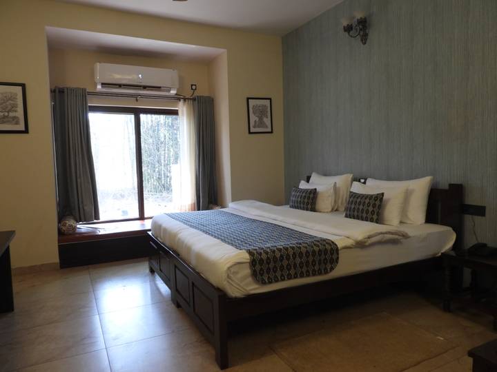 Neatly furnished hotel room with a large bed, wooden furniture and window overlooking greenery.