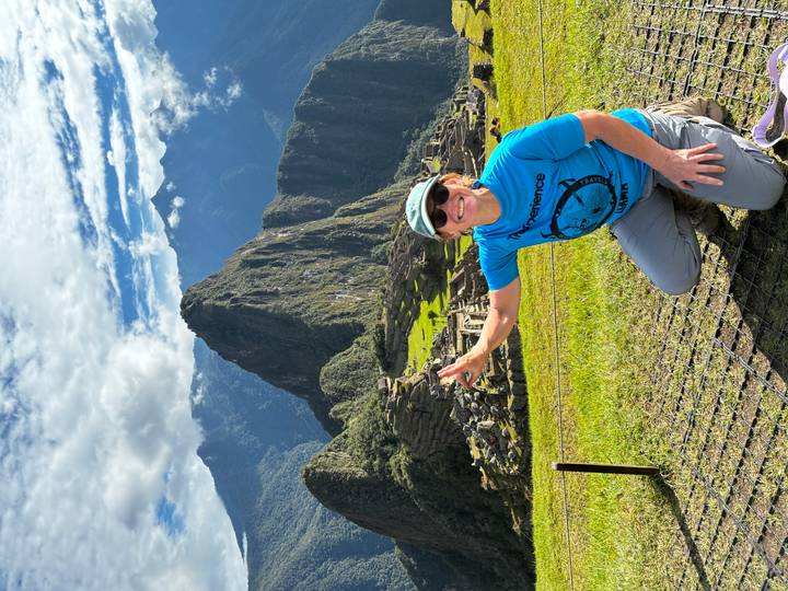 Traveler kneels and flashes a peace sign with Machu Picchu rising majestically behind.