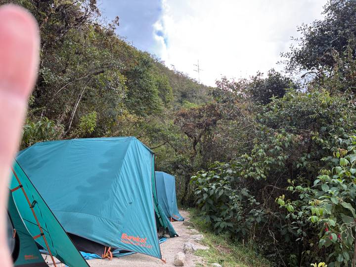 Green camping tents set up along a jungle trail with a finger partially obscuring the lens.