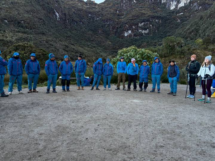 Line of porters and guides in blue uniforms standing together on a clearing along the Inca Trail.