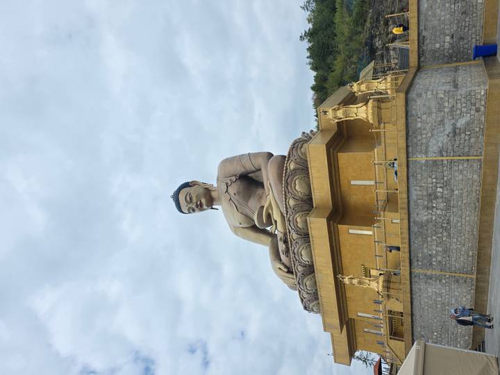 Massive seated golden Buddha statue atop a large pedestal under an overcast sky.
