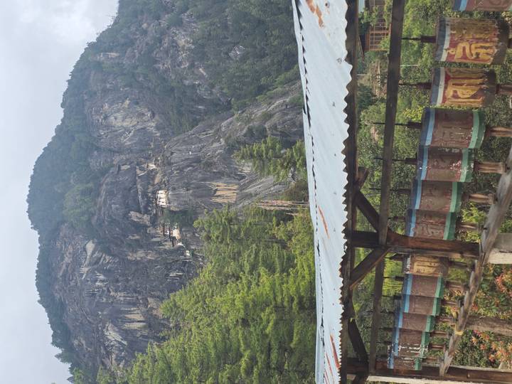Prayer wheels line a covered walkway with Tiger’s Nest monastery clinging high on a cliff in the distance.